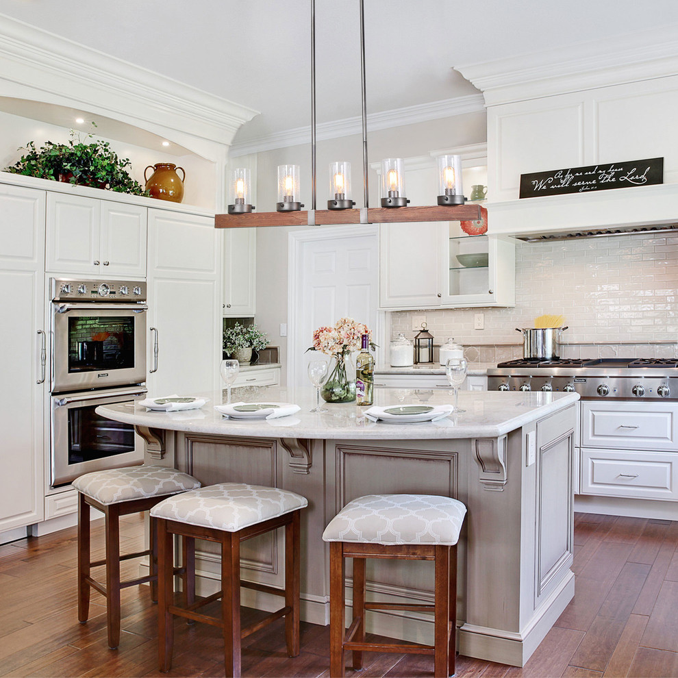 This is an example of a transitional u-shaped kitchen in Other with raised-panel cabinets, white cabinets, white splashback, stainless steel appliances, medium hardwood floors, with island and brown floor.