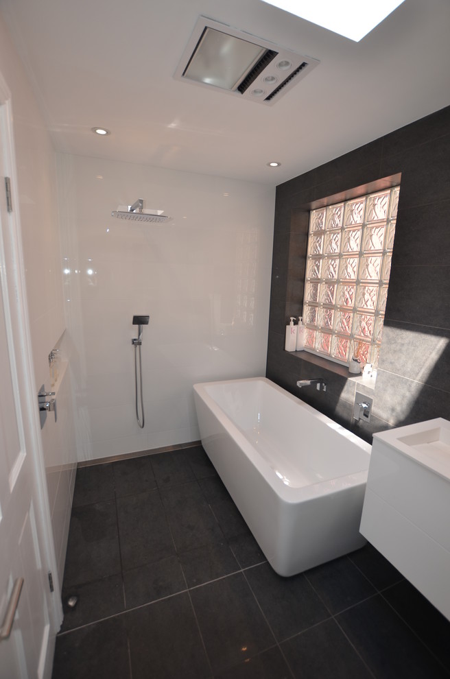 Photo of a contemporary bathroom in Sydney with a wall-mount sink, a freestanding tub, an open shower, flat-panel cabinets, white cabinets, engineered quartz benchtops, black tile and porcelain tile.