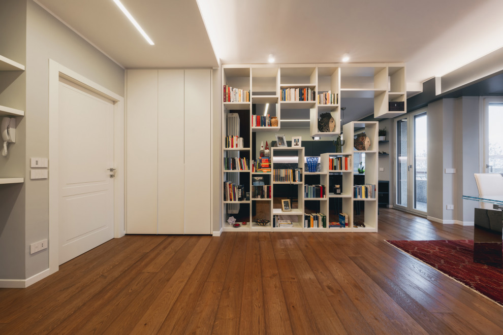 Пример оригинального дизайна: большая открытая гостиная комната в современном стиле с с книжными шкафами и полками, серыми стенами, светлым паркетным полом, мультимедийным центром, коричневым полом и многоуровневым потолком