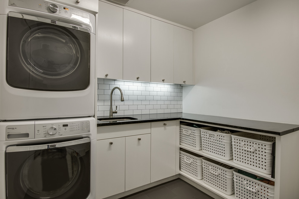 Photo of a mid-sized scandinavian l-shaped dedicated laundry room in Dallas with an undermount sink, flat-panel cabinets, white cabinets, white walls, a stacked washer and dryer, quartz benchtops and ceramic floors.