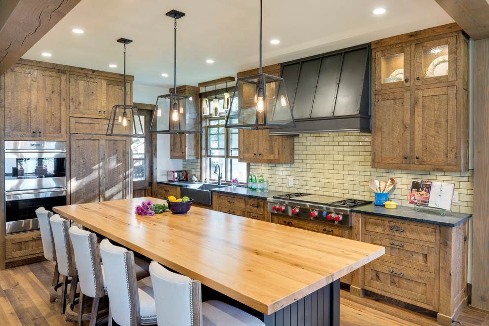 Photo of a country l-shaped kitchen in Minneapolis with a farmhouse sink, shaker cabinets, dark wood cabinets, stainless steel appliances, dark hardwood floors, with island, brown floor and grey benchtop.