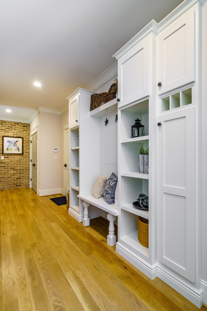 Example of a large transitional medium tone wood floor and brown floor mudroom design with white walls and a medium wood front door