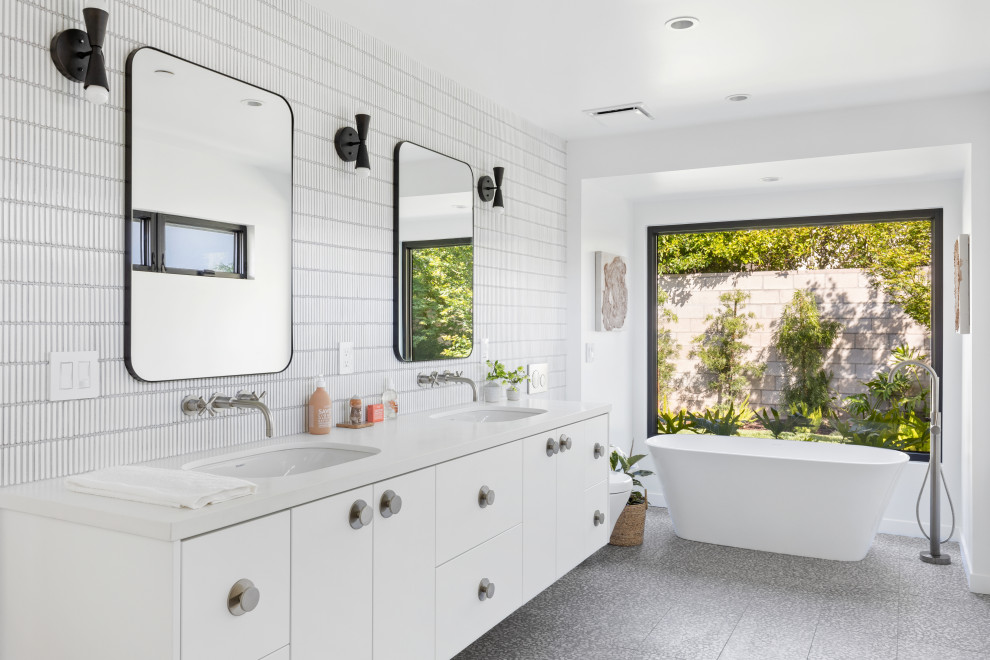 Cette photo montre une salle de bain rétro avec un placard à porte plane, des portes de placard blanches, une baignoire indépendante, un carrelage blanc, un mur blanc, un lavabo encastré, un sol gris, un plan de toilette blanc, meuble double vasque et meuble-lavabo suspendu.