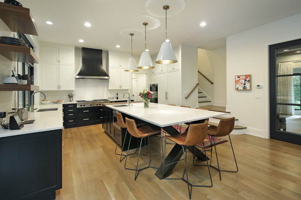 This is an example of a large transitional l-shaped eat-in kitchen in Chicago with an undermount sink, recessed-panel cabinets, black cabinets, quartzite benchtops, white splashback, ceramic splashback, stainless steel appliances, medium hardwood floors, with island, brown floor and white benchtop.