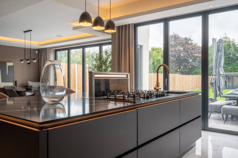 Inspiration for a large modern l-shaped open plan kitchen in Hertfordshire with flat-panel cabinets, black splashback, black appliances, marble floors, with island, black benchtop and recessed.