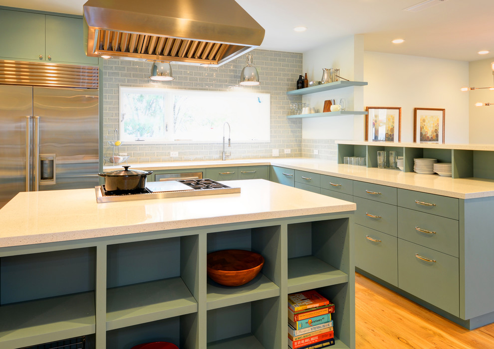 Mid-sized midcentury l-shaped eat-in kitchen in Austin with an undermount sink, flat-panel cabinets, green cabinets, quartz benchtops, grey splashback, ceramic splashback, stainless steel appliances, medium hardwood floors and with island.