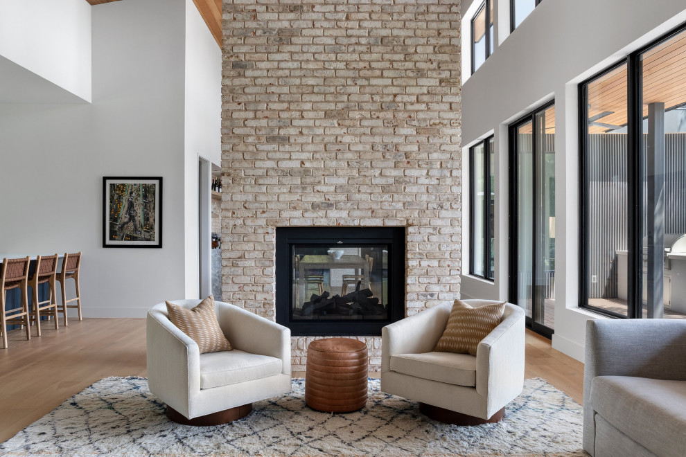 Inspiration for a large midcentury open concept living room in Austin with light hardwood floors, a two-sided fireplace, a brick fireplace surround, a built-in media wall, wood and wood walls.