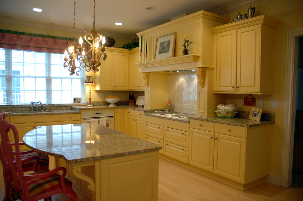 This is an example of a traditional u-shaped eat-in kitchen in Indianapolis with an undermount sink, raised-panel cabinets, yellow cabinets, granite benchtops, white appliances, light hardwood floors and with island.