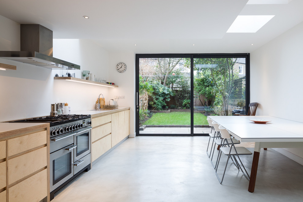 This is an example of a mid-sized contemporary single-wall eat-in kitchen in London with flat-panel cabinets, light wood cabinets, laminate benchtops, no island, white benchtop, stainless steel appliances, concrete floors and grey floor.