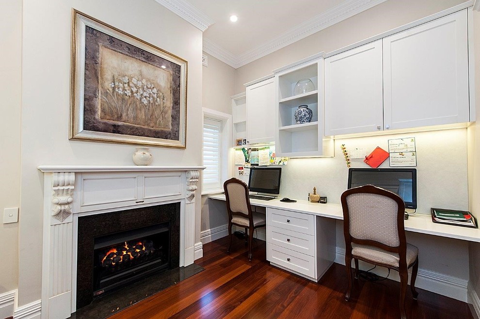 Photo of a mid-sized traditional study room in Perth with dark hardwood floors, a standard fireplace, a plaster fireplace surround and a built-in desk.