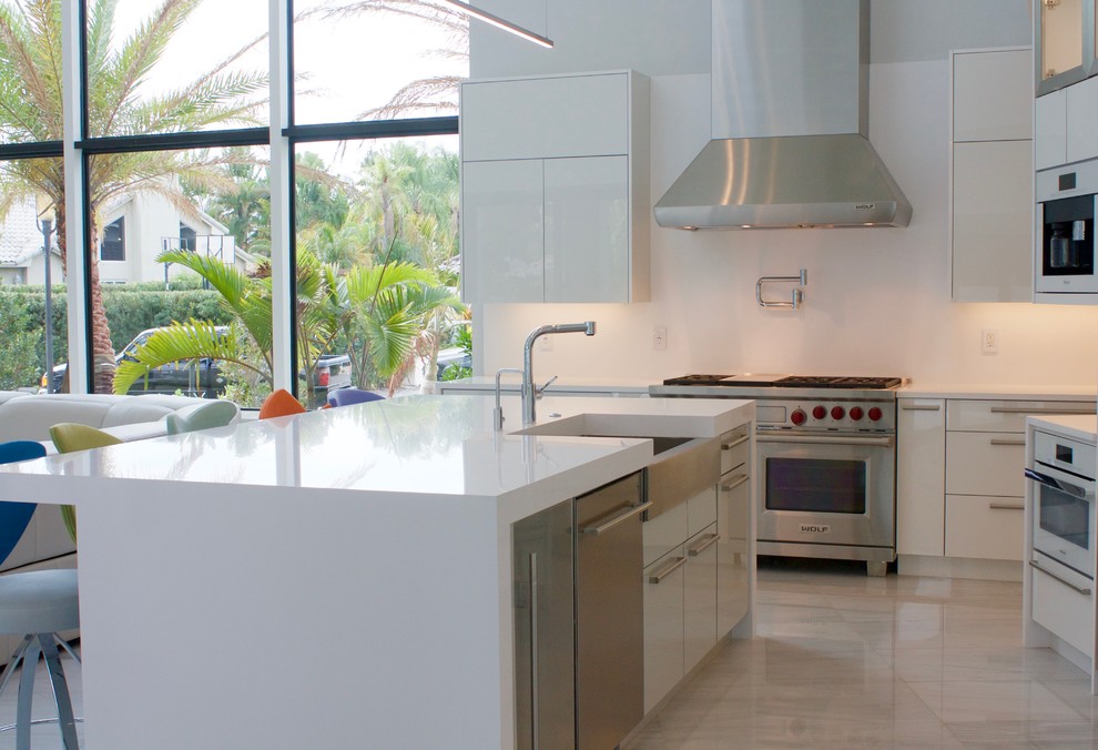 Large contemporary u-shaped open plan kitchen in Miami with a farmhouse sink, flat-panel cabinets, white cabinets, quartz benchtops, white splashback, stainless steel appliances, marble floors and with island.