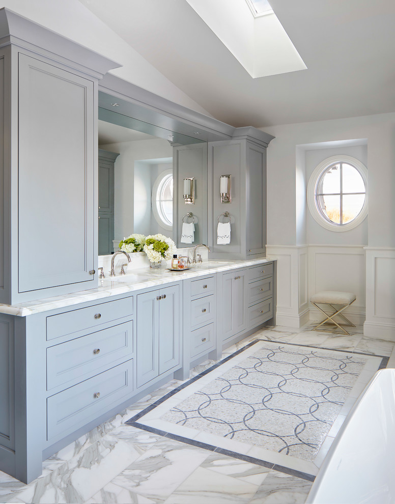 Inspiration for a large contemporary master bathroom in Denver with recessed-panel cabinets, grey cabinets, a freestanding tub, white tile, marble, grey walls, marble floors, an undermount sink, marble benchtops, white floor and white benchtops.