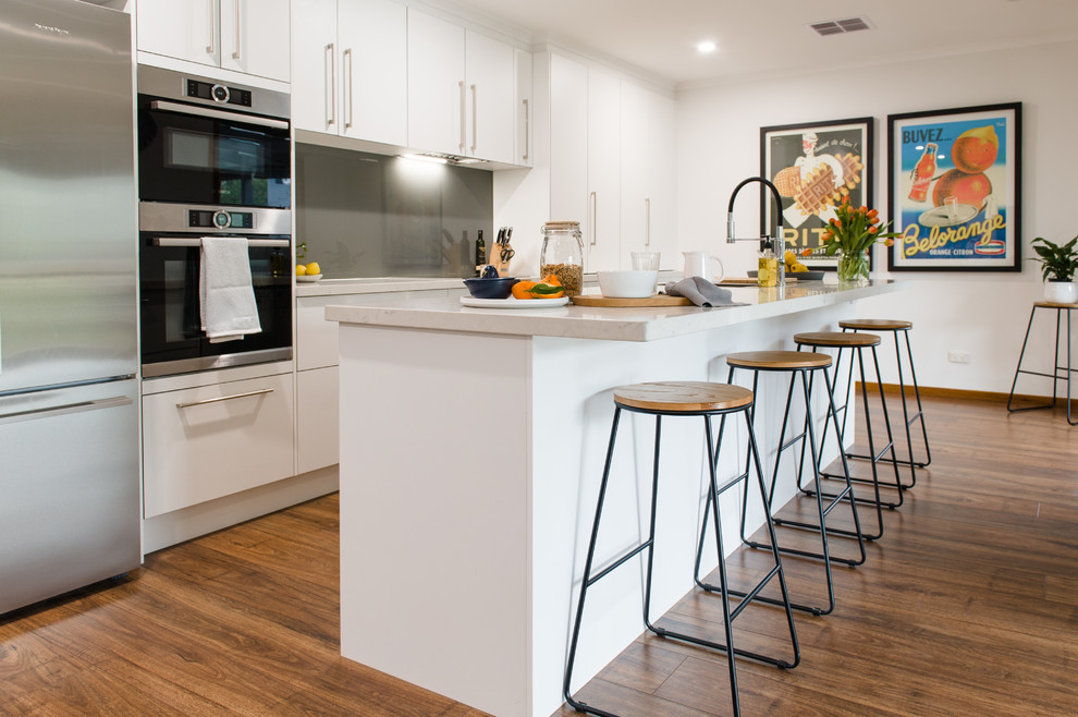 Large contemporary u-shaped kitchen in Melbourne with a double-bowl sink, open cabinets, white cabinets, quartz benchtops, metallic splashback, glass sheet splashback, stainless steel appliances, medium hardwood floors, with island and beige benchtop.