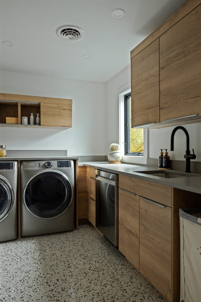 Inspiration for a rustic l-shaped vinyl floor laundry room remodel with an undermount sink, flat-panel cabinets, medium tone wood cabinets, solid surface countertops, a side-by-side washer/dryer and gray countertops