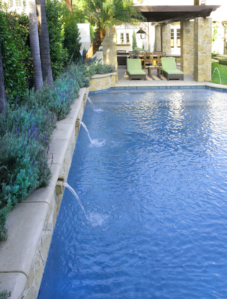 Diseño de piscina con fuente alargada mediterránea grande rectangular en patio trasero con losas de hormigón