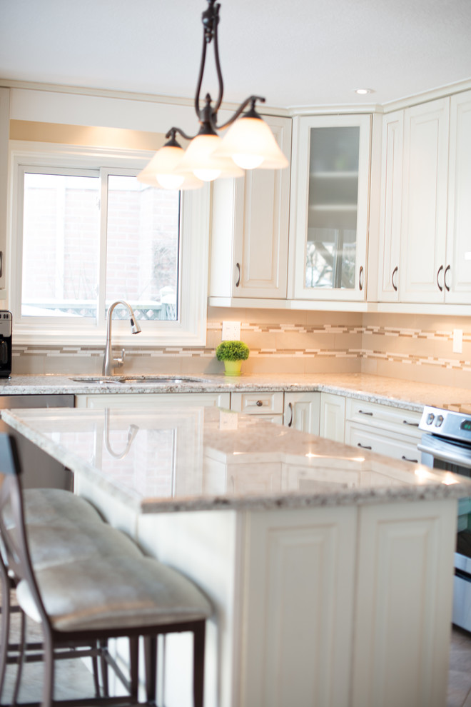 Traditional kitchen in Toronto with a double-bowl sink, raised-panel cabinets, white cabinets, granite benchtops, beige splashback, glass tile splashback, stainless steel appliances and vinyl floors.