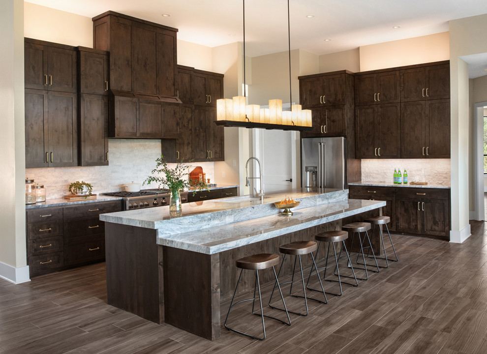 Example of a large transitional l-shaped dark wood floor and brown floor open concept kitchen design in Austin with an undermount sink, shaker cabinets, dark wood cabinets, quartzite countertops, gray backsplash, stone tile backsplash, stainless steel appliances, an island and gray countertops