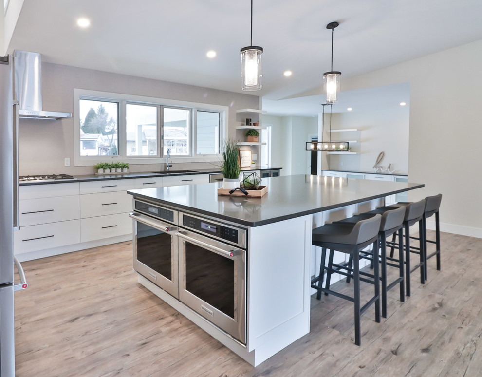 Open concept kitchen - large transitional l-shaped vinyl floor and brown floor open concept kitchen idea with an undermount sink, flat-panel cabinets, white cabinets, quartz countertops, gray backsplash, porcelain backsplash, stainless steel appliances and an island