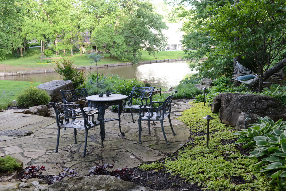 This is an example of a large traditional backyard patio in St Louis with natural stone pavers and no cover.