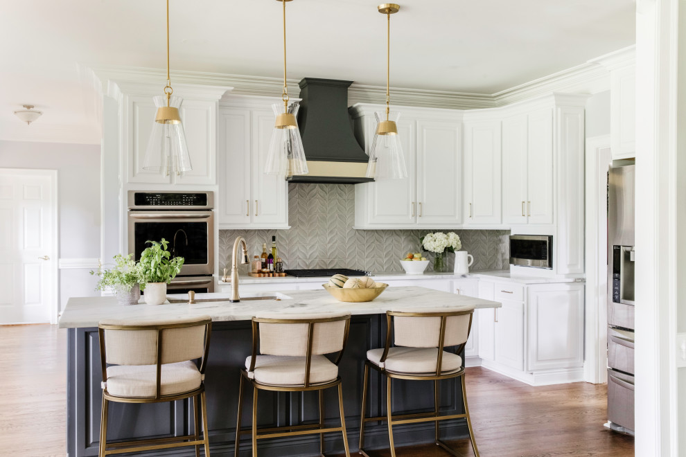 Bild på ett mellanstort vintage vit linjärt vitt kök och matrum, med en undermonterad diskho, luckor med upphöjd panel, vita skåp, marmorbänkskiva, grått stänkskydd, stänkskydd i keramik, rostfria vitvaror, mellanmörkt trägolv, en köksö och brunt golv