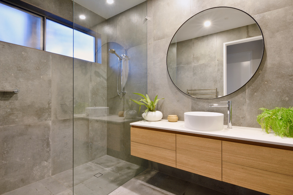 Beach style bathroom in Sunshine Coast with flat-panel cabinets, medium wood cabinets, a curbless shower, gray tile, a vessel sink, grey floor and an open shower.