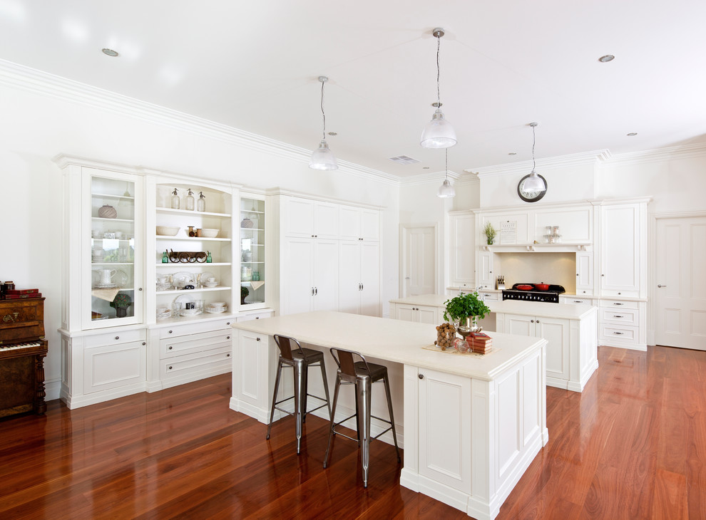 Inspiration for a transitional eat-in kitchen in Melbourne with a farmhouse sink, shaker cabinets, white cabinets, black appliances, medium hardwood floors and multiple islands.