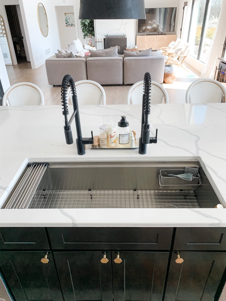 This is an example of a large galley eat-in kitchen in Austin with an undermount sink, shaker cabinets, black cabinets, quartz benchtops, white splashback, engineered quartz splashback, stainless steel appliances, medium hardwood floors, with island, brown floor and white benchtop.