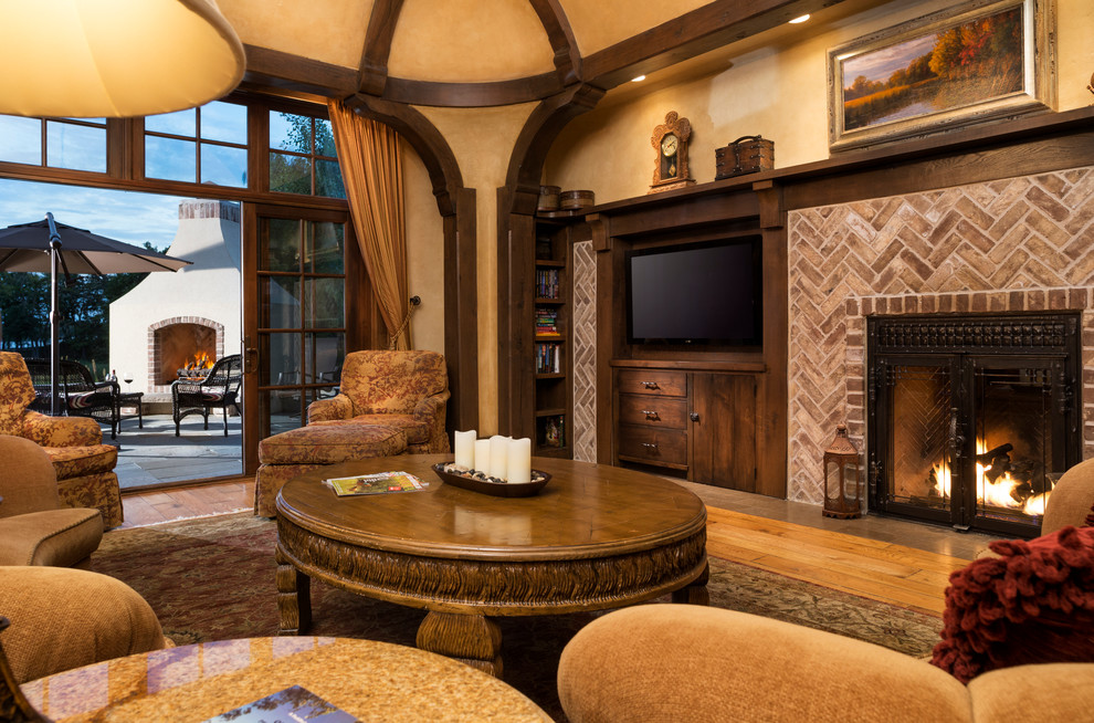 This is an example of a large traditional open concept living room in Minneapolis with medium hardwood floors, a standard fireplace, a brick fireplace surround, beige walls and a concealed tv.