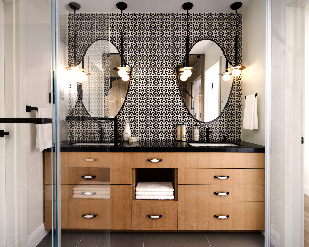 This is an example of a mid-sized modern master bathroom in Atlanta with flat-panel cabinets, medium wood cabinets, a double shower, a one-piece toilet, black and white tile, ceramic tile, pebble tile floors, an undermount sink, granite benchtops, grey floor, a hinged shower door, black benchtops, a shower seat, a double vanity and a built-in vanity.