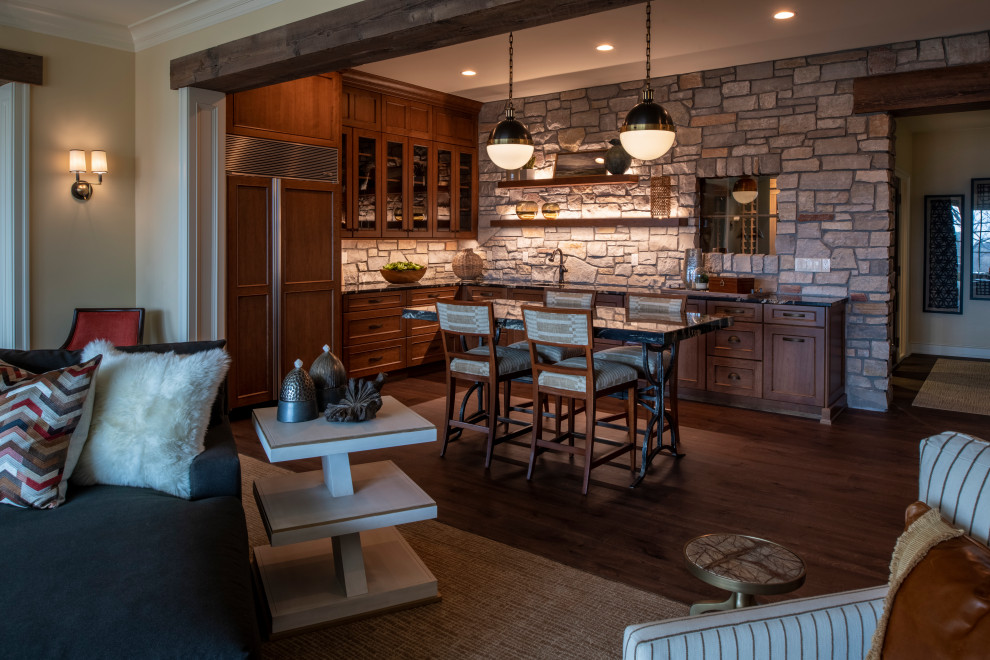 This is an example of a large traditional l-shaped wet bar in Minneapolis with an undermount sink, recessed-panel cabinets, dark wood cabinets, grey splashback, limestone splashback, dark hardwood floors, brown floor and black benchtop.