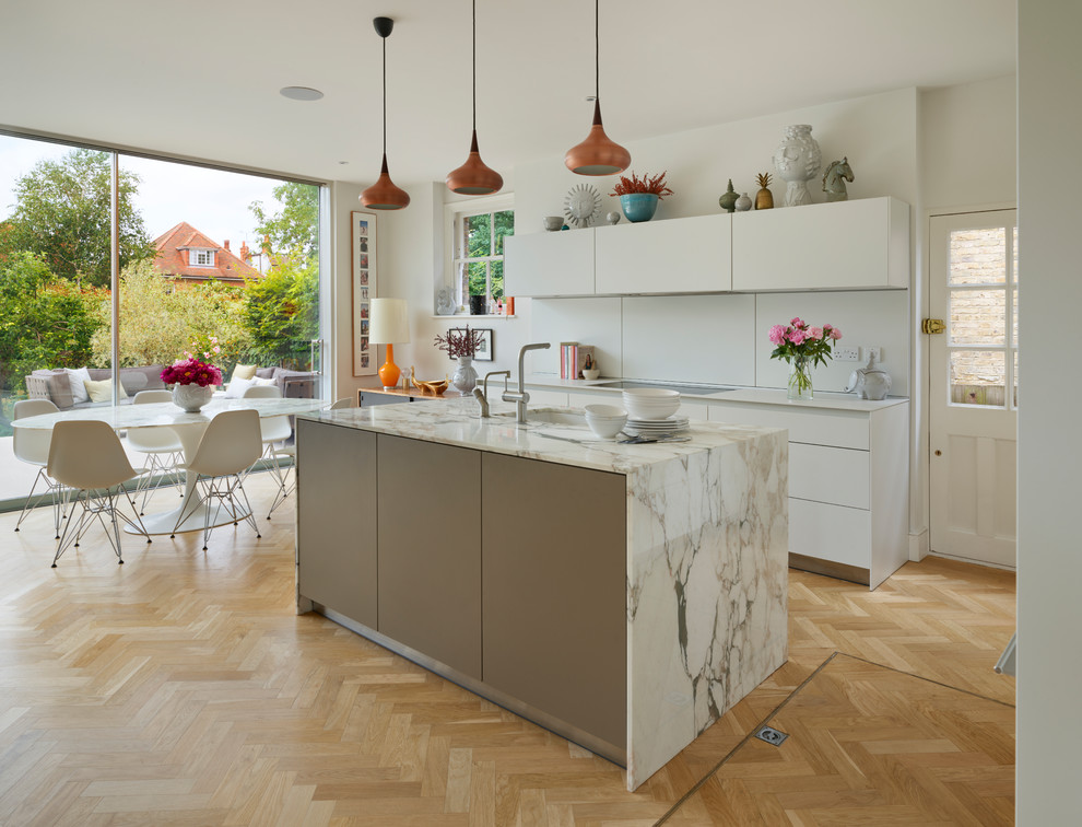 Design ideas for a mid-sized contemporary l-shaped eat-in kitchen in Other with an undermount sink, flat-panel cabinets, white cabinets, marble benchtops, white splashback, white appliances, light hardwood floors, with island and beige floor.