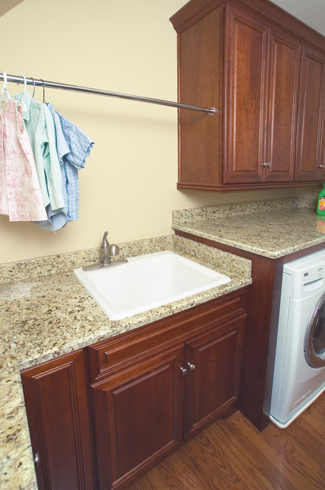 Photo of a mid-sized traditional l-shaped dedicated laundry room in Atlanta with an undermount sink, raised-panel cabinets, dark wood cabinets, granite benchtops, grey walls, porcelain floors and a side-by-side washer and dryer.