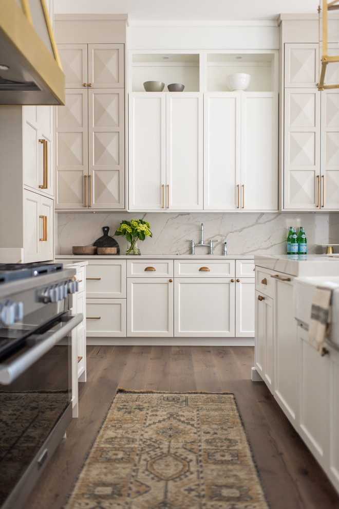 Huge transitional u-shaped medium tone wood floor and brown floor open concept kitchen photo in Indianapolis with a farmhouse sink, shaker cabinets, white cabinets, quartzite countertops, white backsplash, stone slab backsplash, stainless steel appliances and two islands