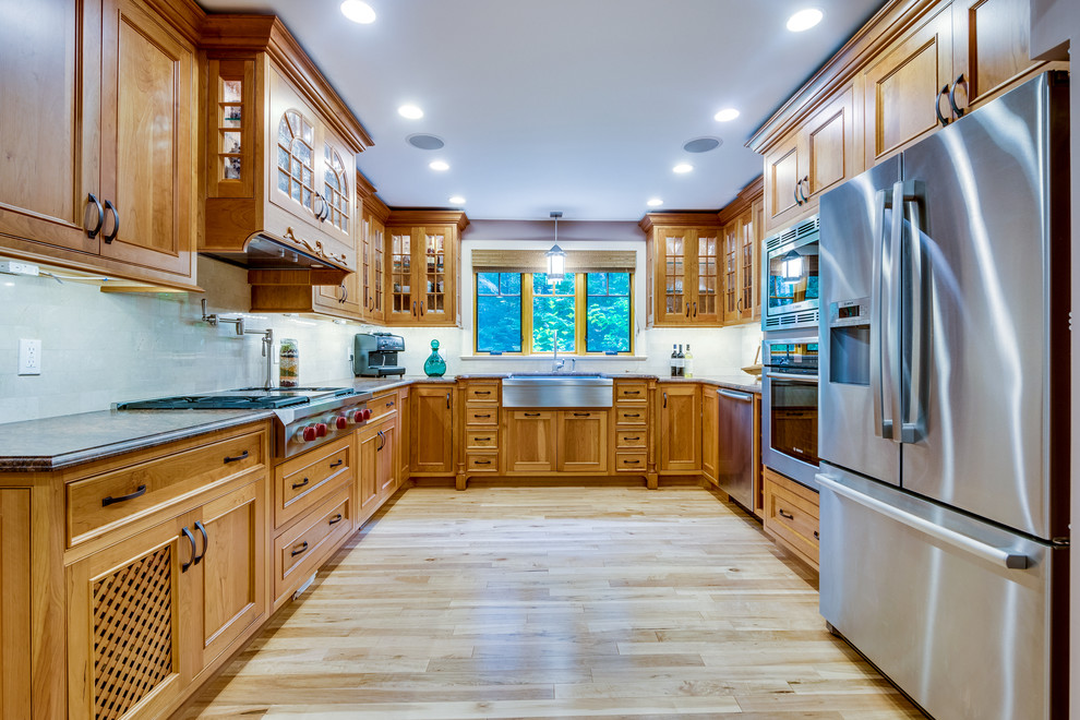 Mid-sized transitional u-shaped medium tone wood floor and brown floor enclosed kitchen photo in Boston with a farmhouse sink, recessed-panel cabinets, medium tone wood cabinets, granite countertops, beige backsplash, stone tile backsplash, stainless steel appliances and no island