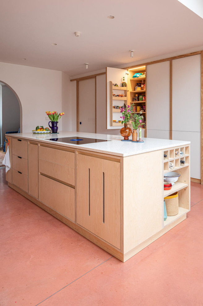 Пример оригинального дизайна: большая параллельная кухня-гостиная в современном стиле с плоскими фасадами, светлыми деревянными фасадами, бетонным полом, островом и розовым полом
