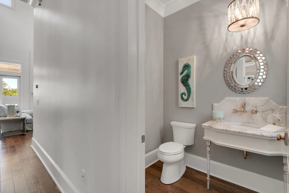 Photo of a large country powder room in Other with a one-piece toilet, grey walls, medium hardwood floors, a pedestal sink, marble benchtops and open cabinets.