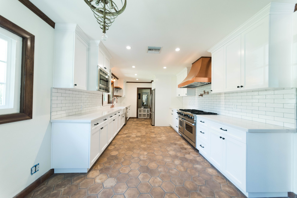 This is an example of a mid-sized industrial u-shaped eat-in kitchen in San Francisco with a farmhouse sink, flat-panel cabinets, white cabinets, quartzite benchtops, ceramic splashback, stainless steel appliances, terra-cotta floors and brown floor.