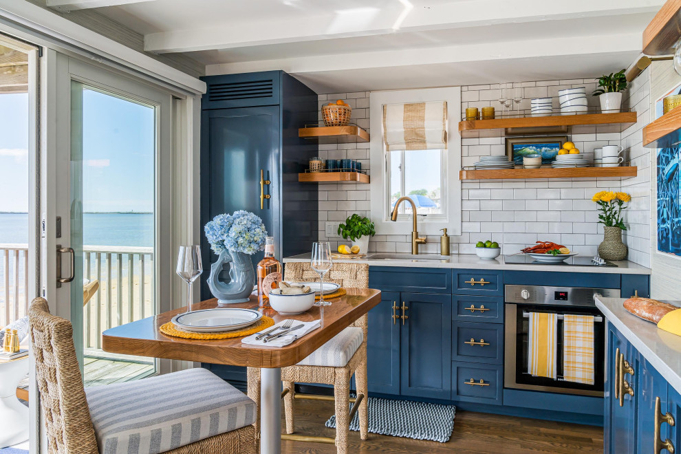 Small beach style l-shaped eat-in kitchen in Boston with an undermount sink, shaker cabinets, blue cabinets, white splashback, white benchtop, subway tile splashback, stainless steel appliances, dark hardwood floors, with island, brown floor and exposed beam.