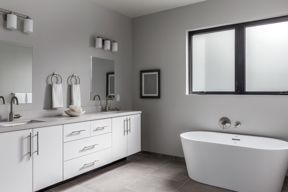 Photo of a large contemporary master bathroom in San Diego with flat-panel cabinets, white cabinets, a freestanding tub, a corner shower, a one-piece toilet, gray tile, glass tile, grey walls, ceramic floors, an undermount sink, engineered quartz benchtops, grey floor, a hinged shower door and grey benchtops.