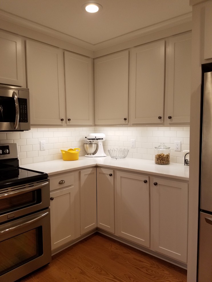 Mid-sized transitional u-shaped medium tone wood floor and brown floor eat-in kitchen photo with an undermount sink, shaker cabinets, white cabinets, quartz countertops, white backsplash, subway tile backsplash, stainless steel appliances and a peninsula