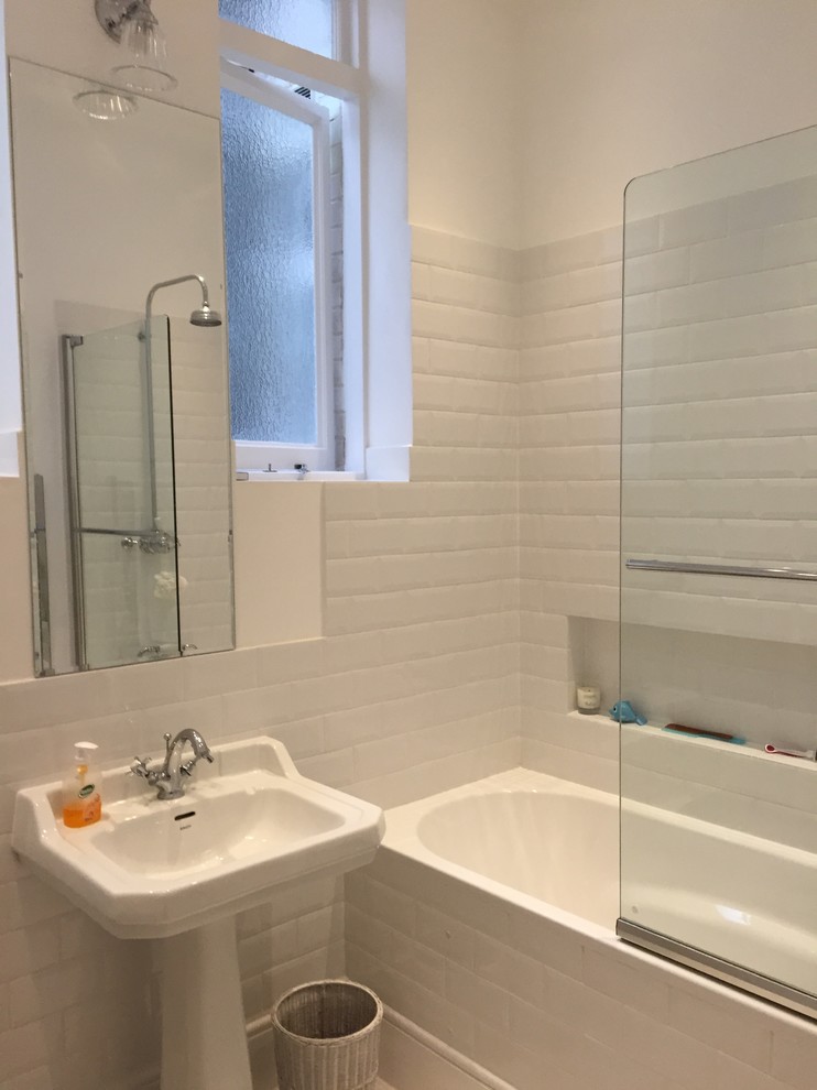 Photo of a small traditional master bathroom in London with a pedestal sink, a shower/bathtub combo, white tile, ceramic tile, white walls, ceramic floors, a drop-in tub and a one-piece toilet.