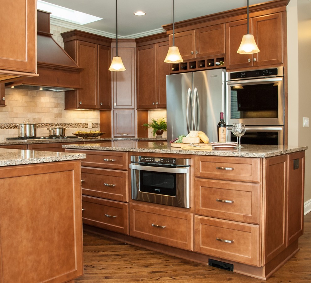 Large traditional u-shaped eat-in kitchen in Detroit with an undermount sink, recessed-panel cabinets, medium wood cabinets, quartz benchtops, brown splashback, subway tile splashback, stainless steel appliances, medium hardwood floors and with island.