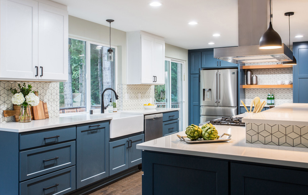Design ideas for a mid-sized country u-shaped open plan kitchen in Seattle with a farmhouse sink, shaker cabinets, white cabinets, quartz benchtops, white splashback, ceramic splashback, stainless steel appliances, medium hardwood floors, a peninsula, brown floor and white benchtop.