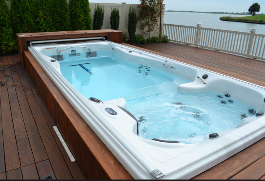 Large traditional backyard rectangular lap pool in Other with a hot tub and decking.
