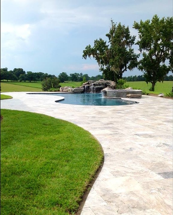 Design ideas for a large tropical backyard kidney-shaped lap pool in Other with natural stone pavers.
