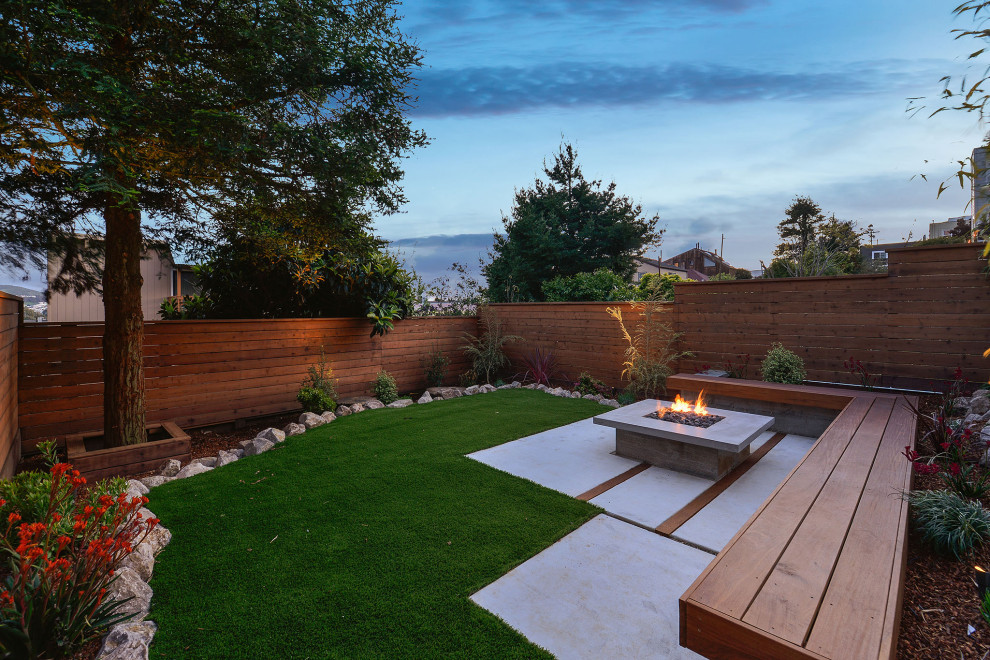 This is an example of a medium sized contemporary back xeriscape full sun garden in San Francisco with a fire feature, concrete paving and a wood fence.