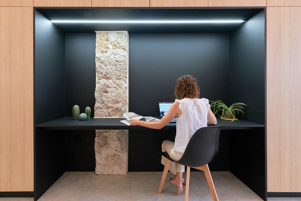 This is an example of a mid-sized modern home studio in Alicante-Costa Blanca with black walls, concrete floors, a built-in desk, grey floor, exposed beam and panelled walls.