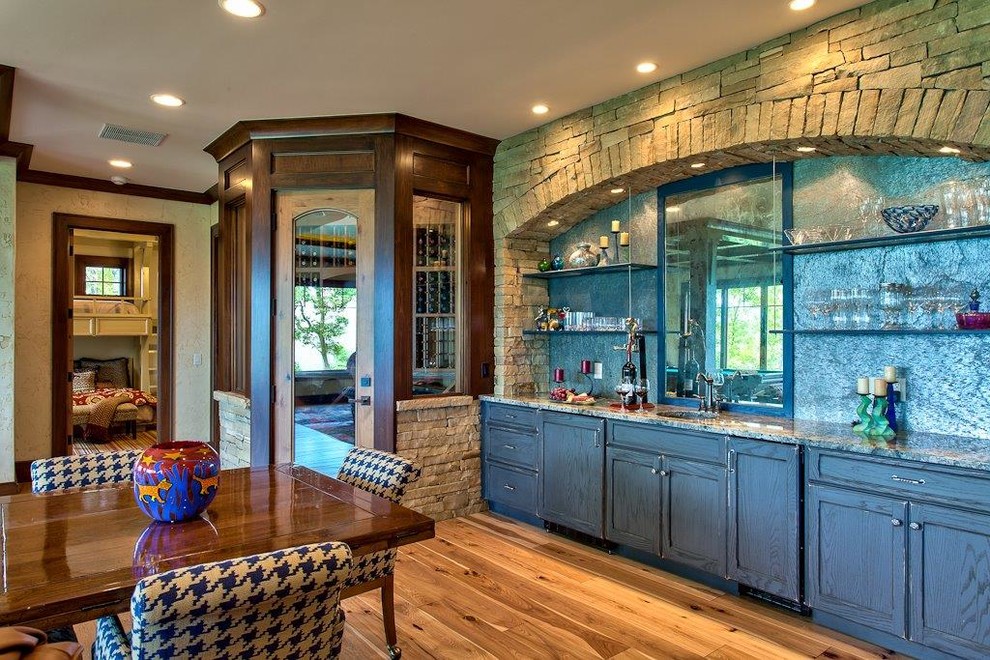 Inspiration for a mid-sized country single-wall wet bar in Other with an undermount sink, recessed-panel cabinets, distressed cabinets, granite benchtops, grey splashback, stone slab splashback, light hardwood floors, brown floor and grey benchtop.