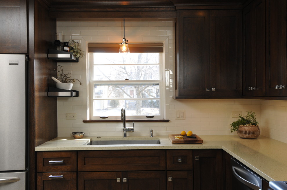 Photo of a small midcentury galley eat-in kitchen in Chicago with a single-bowl sink, shaker cabinets, dark wood cabinets, quartz benchtops, white splashback, ceramic splashback, stainless steel appliances, limestone floors and with island.