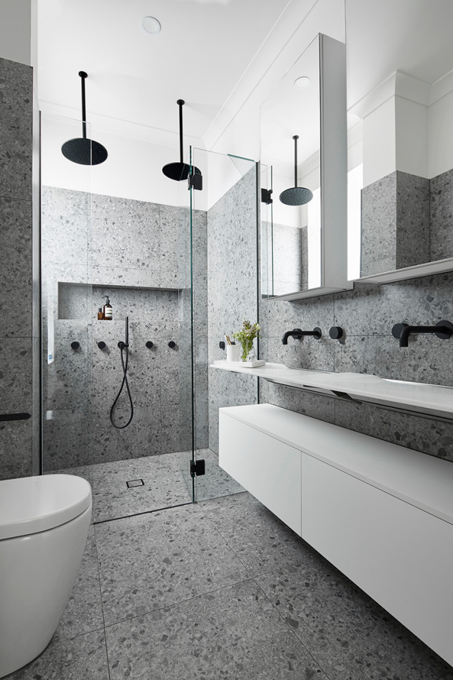 Mid-sized contemporary master bathroom in Melbourne with white cabinets, a double shower, a wall-mount toilet, gray tile, stone slab, grey walls, terrazzo floors, a wall-mount sink, laminate benchtops, grey floor, a hinged shower door, white benchtops and flat-panel cabinets.